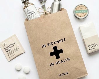 May include: A brown paper bag printed with IN SICKNESS + IN HEALTH and 10.28.22, containing a Wellness Tea Blend bottle, a silver dropper bottle, and lavender. Includes a Mint & Honey lip balm, tissues, immune support packet, and three white tablets.