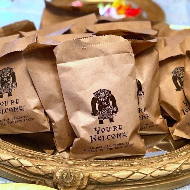 May include: Brown paper bags with a cartoon character printed on them. The bags have the text "You're Welcome! Thanks for coming to Aloha's 1st Birthday Party" printed on them.