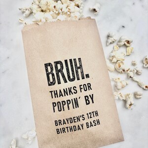 May include: A brown paper bag filled with popcorn, with some popcorn spilling out. The bag has the text "BRUH. THANKS FOR POPPIN' BY BRAYDEN'S 12TH BIRTHDAY BASH" printed in black.