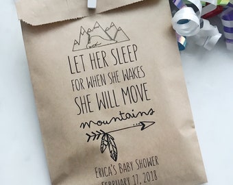May include: A brown paper bag with a white clip, featuring black text and illustrations. The text reads "LET HER SLEEP FOR WHEN SHE WAKES SHE WILL MOVE mountains." Below is "ERICA'S BABY SHOWER FEBRUARY 17, 2018."