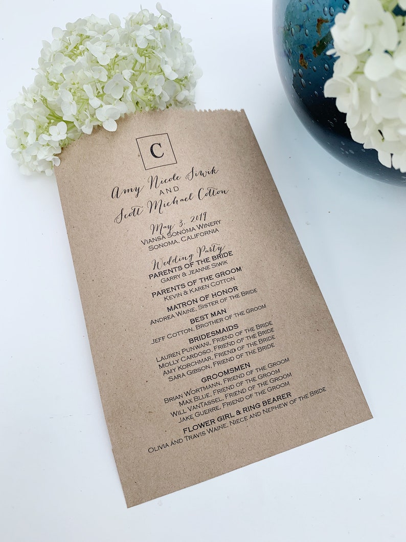 Peut inclure: Un programme de mariage en papier brun avec du texte noir. Le programme &eacute;num&egrave;re les noms des mari&eacute;s, la date, le lieu et le cort&egrave;ge nuptial. Des fleurs blanches sont en arri&egrave;re-plan.