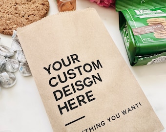 May include: A brown paper bag with the text "YOUR CUSTOM DESIGN HERE ANYTHING YOU WANT!" printed on it. The bag is filled with various items, including a bottle of Jack Daniel's Tennessee Apple liqueur, a bag of chocolate chip cookies, and a bag of chocolate candies.
