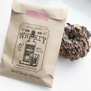 Puede incluir: Una bolsa de papel marr&oacute;n con una pegatina a rayas rojas y blancas. La bolsa tiene un gr&aacute;fico en blanco y negro de una botella de whisky, un vaso y un cigarro con el texto "Single Barreled Est. 1978 Whiskey 40 Years Old 40% Alc/Vol Limited Edition Thank You for Coming".