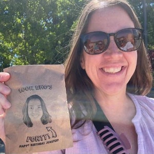 Puede incluir: Una tarjeta marr&oacute;n con el texto "Look Who's Forty! Happy Birthday Jenifer!" y una foto de una mujer con cabello casta&ntilde;o.