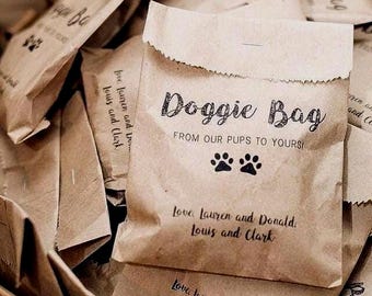 May include: A collection of small, brown paper bags labeled "Doggie Bag" with paw print graphics. The bags are printed with the text "From Our Pups to Yours!" and names. The bags are folded and appear to be filled.