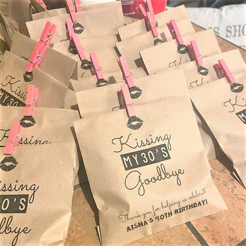 Puede incluir: Bolsas de papel marr&oacute;n con pinzas de ropa rosas y texto negro que dice "Kissing My 30's Goodbye" y "&iexcl;Gracias por ayudarnos a celebrar el 40 cumplea&ntilde;os de Aisha!"