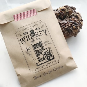 Puede incluir: Una bolsa de papel marr&oacute;n con una cinta de rayas rojas y blancas. La bolsa tiene un gr&aacute;fico en blanco y negro de una botella de whisky, un vaso y un cigarro con el texto "Single Barred Est. 1978 Whiskey 40 Years Old 40% Alc/Vol Limited Edition Thank You for Coming".