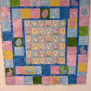 May include: A patchwork quilt with a central panel featuring a repeating pattern of bunnies and eggs. The quilt is made with a variety of fabrics in shades of pink, blue, green, and yellow.