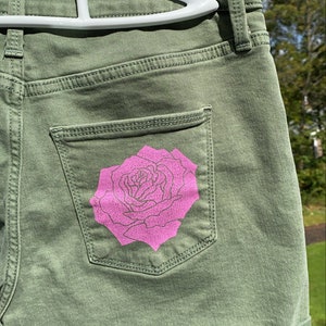 May include: Green denim shorts with a pink rose design on the back pocket.