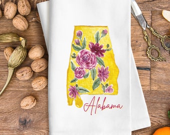 Peut inclure: Une serviette de cuisine blanche avec un contour jaune de l'état d'Alabama avec des motifs floraux roses et verts. Le texte "Alabama" est écrit en cursive rose sous le contour de l'état.