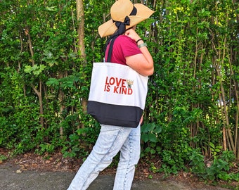 Peut inclure: Une personne portant une chemise rouge, un chapeau de paille avec un ruban noir et un jean bleu porte un sac fourre-tout blanc avec des anses noires. Le sac porte l'inscription "LOVE IS KIND" imprimée en rouge.
