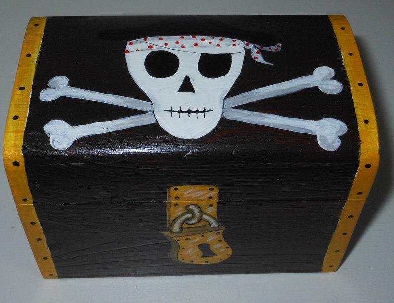 May include: A black wooden treasure chest with a pirate theme. The chest features a white skull with a red-spotted bandana and crossed bones. The edges are trimmed in yellow, and a gold-colored lock is on the front.