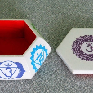 May include: White hexagonal box with a red interior and a lid featuring a purple chakra symbol with the Sanskrit word "Om". The box is decorated with colorful chakra symbols.