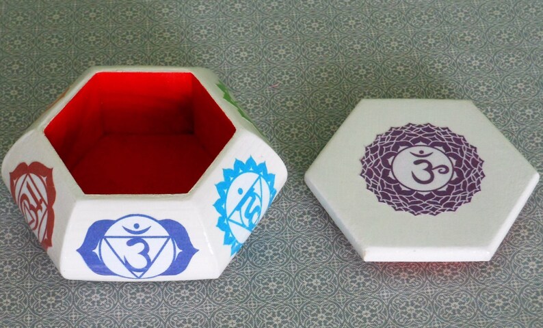 May include: White hexagonal box with a red interior and a lid featuring a purple chakra symbol with the Sanskrit word "Om". The box is decorated with colorful chakra symbols.