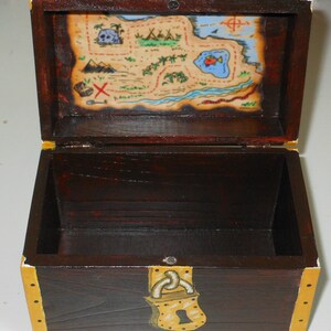 May include: A wooden treasure chest with a dark brown finish, gold accents, and a painted treasure map on the inside lid. The chest is open, revealing the interior. The map features a skull, palm trees, and a red 'X' marking the spot.