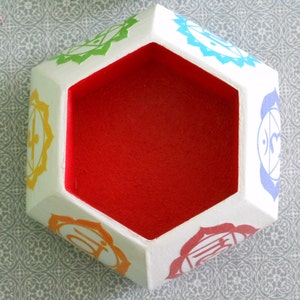 May include: White hexagonal box with a red interior. The box has seven colorful symbols on each side, representing the seven chakras.