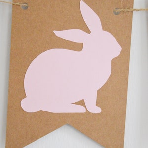 May include: A brown paper banner with a light pink bunny silhouette. The banner is suspended by a natural twine string. The bunny is in a seated position, with its ears upright. This banner is perfect for Easter or spring decor.