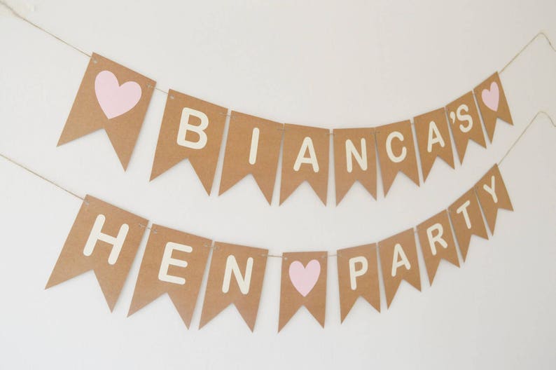 May include: A brown paper banner with white letters spelling "Bianca's Hen Party" with pink hearts between the words.