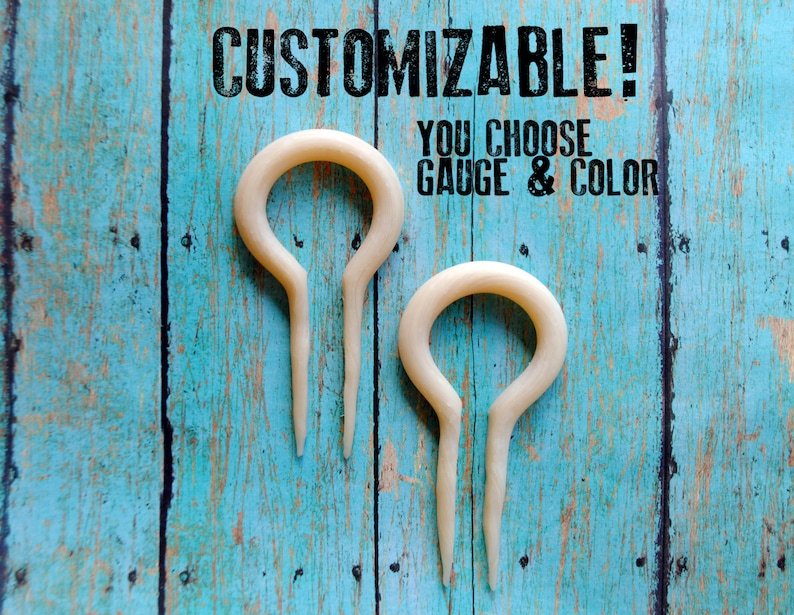 May include: Two white bone ear gauges, shaped like a teardrop with a loop at the top. The text "CUSTOMIZABLE! YOU CHOOSE GAUGE & COLOR" is above the gauges.