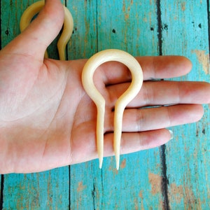 May include: A pair of white bone hair forks with a rounded loop at the top and two prongs at the bottom.