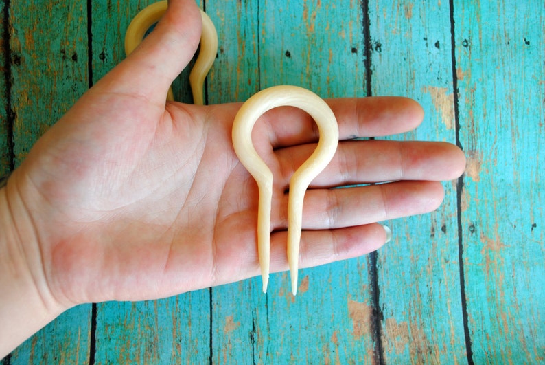 May include: A pair of white bone hair forks with a rounded loop at the top and two prongs at the bottom.