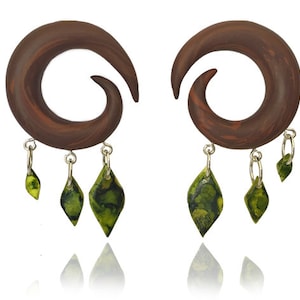 May include: A pair of brown wooden spiral ear gauges with dangling green and black marbled teardrop charms.