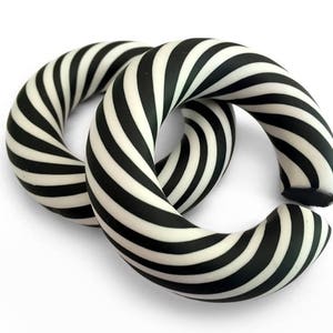 May include: Two black and white striped hoop earrings. The stripes are thick and swirl around the hoop.