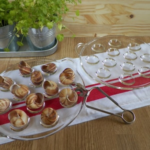 Può includere: Due piatti da portata in vetro trasparente per lumache. Un piatto ha 12 incavi individuali per le lumache. L'altro piatto ha 12 lumache disposte in cerchio.