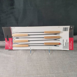 May include: A package of six fondue forks with wooden handles. The forks are made of stainless steel and have a two-pronged design. The package is white with black text and a barcode.