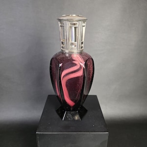 May include: A deep purple glass fragrance lamp with a faceted, teardrop-shaped body featuring swirling pink accents and a metallic silver-toned openwork crown top. The vessel has a hexagonal base and a smooth, reflective finish throughout.