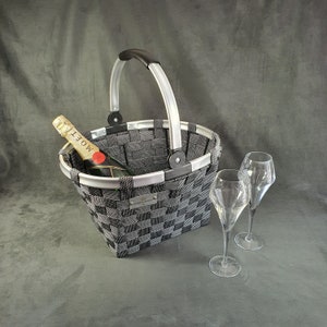 May include: A black and silver woven basket with a black handle. A bottle of Moët champagne is inside the basket. Two clear glass champagne flutes are on the gray surface.