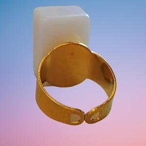 May include: A gold-toned adjustable ring featuring a smooth, rectangular, opaque white stone setting. The metal band has a polished finish and an open design at the back, allowing for size adjustments to fit various finger widths comfortably.