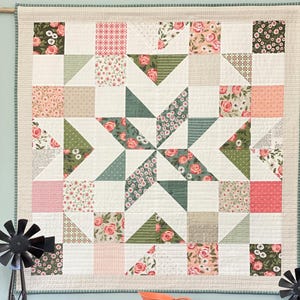 May include: A white quilt with a starburst pattern made from various floral fabric squares in shades of pink, green, and white.