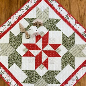 May include: A red and green quilted table runner with a starburst design. The runner has a white background with red and green fabric squares. The border is red with white polka dots and a green leaf pattern. The text "Fresh Dew Drops" is visible in the bottom right corner.