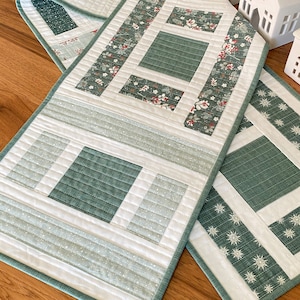 Peut inclure: Un chemin de table matelassé blanc et vert avec un motif géométrique. Le chemin de table a un fond blanc avec des carrés et des rectangles verts. Le chemin de table est bordé d'une bordure verte.