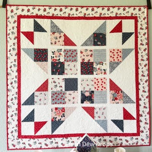 Könnte beinhalten: Eine handgefertigte Steppdecke mit weißem Hintergrund, mit roten, marineblauen und floral gemusterten Quadraten und Dreiecken. Die Steppdecke hat einen roten Rand mit floralen Akzenten und eine weiße, gesteppte Mitte. Das Gesamtdesign ist geometrisch und traditionell.