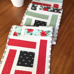 K&ouml;nnte beinhalten: Ein Set aus vier gesteppten Tischl&auml;ufern im Weihnachtsdesign. Die L&auml;ufer haben ein geometrisches Muster in Rot und Wei&szlig; mit schwarzen Akzenten. Der Stoff hat einen festlichen Weihnachtsdruck mit Weihnachtssternen und Stechpalmen.