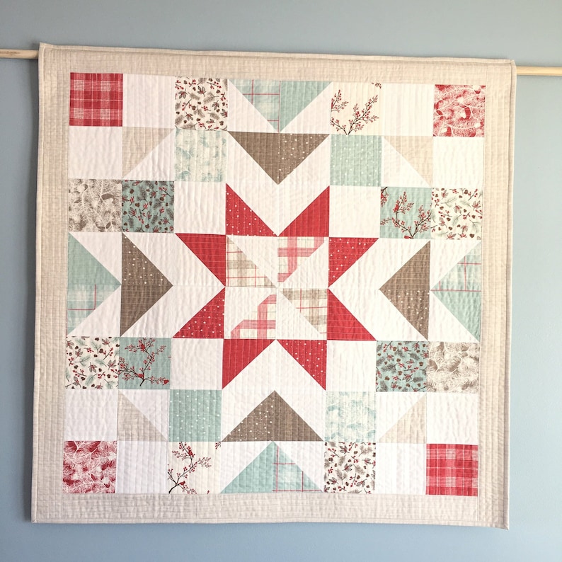 May include: A beige and white quilted wall hanging with a red and white star design. The star is made up of smaller squares in various patterns, including red and white plaid, brown and white floral, and green and white floral. The wall hanging is framed with a beige border.
