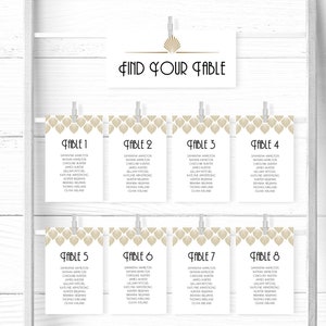 Puede incluir: Un conjunto de ocho tarjetas de mesa con patrones geométricos dorados y blancos. Cada tarjeta tiene un número de mesa y una lista de nombres. Las tarjetas están colgadas en una pared blanca con pinzas para la ropa. El texto en la tarjeta superior dice "Encuentra tu mesa".