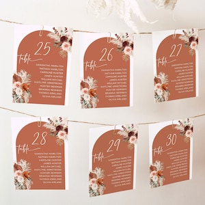 May include: Set of six table number cards with a terracotta background and floral illustrations. The numbers are 25, 26, 27, 28, 29, and 30. Each card has a list of names underneath the number.