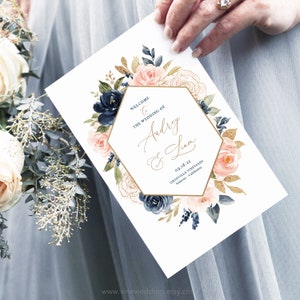 May include: Wedding program with a gold hexagonal frame and watercolor floral design in shades of blue, pink, and gold. The text reads "Welcome to the wedding of Audrey & Liam 09.18.23 Granville Vineyard Sonoma, California".