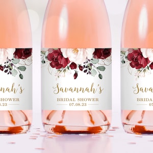 Könnte beinhalten: Drei Weinflaschen mit Etiketten, die ein Blumenmuster in den Farben Burgunderrot, Weiß und Grün zeigen. Die Etiketten enthalten auch den Text "Savannah's Bridal Shower 07.08.23".