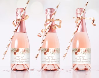 Op de afbeelding: Drie mini champagneflessen met goud-wit gestreepte rietjes en gouden lint. Elke fles heeft een wit etiket met een bloemenontwerp en de tekst "Paisley's Bridal Shower" in gouden schrift. De tekst "Bedankt voor het vieren met ons" staat ook op het etiket.