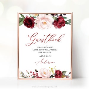 May include: A white sign with a burgundy floral border and the text "Guestbook" in cursive. The sign also includes the text "Please sign and leave your well wishes for the new Mr & Mrs Anderson".