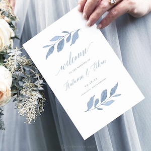 May include: A white wedding program with blue watercolor leaves and the text "Welcome to the wedding of Autumn & Ethan 09.18.23 Charlotte, North Carolina"