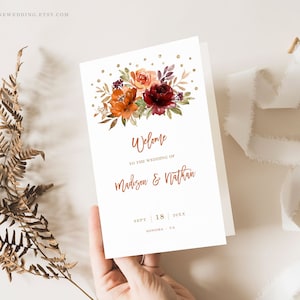 Peut inclure: Invitation de mariage avec un design floral en tons bordeaux, orange et or. Le texte indique "Bienvenue au mariage de Madison & Nathan", la date est le 18 septembre 20XX et le lieu est Sonoma, Californie.