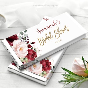 Puede incluir: Dos envoltorios de barra de chocolate blanco con un diseño floral en tonos burdeos y rosa. El texto en el envoltorio dice "Savannah's Bridal Shower 07.18.23".
