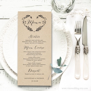 Può includere: Un menu di nozze rustico di colore marrone con un design floreale a forma di cuore nero. Il menu include opzioni di antipasto, piatto principale e dessert. La carta include anche i nomi Savannah & Nathan e la data 10.18.23.