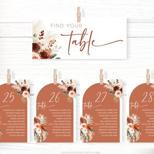 Puede incluir: Conjunto de cuatro tarjetas de n&uacute;mero de mesa de color terracota con un dise&ntilde;o floral. Cada tarjeta presenta un n&uacute;mero de mesa diferente, del 25 al 28, y una lista de nombres para cada mesa. Las tarjetas tienen una forma de arco redondeado y est&aacute;n decoradas con un arreglo floral de flores burdeos, melocot&oacute;n y blancas, junto con hierba de la pampa beige.