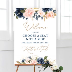 May include: A white wedding sign with blue and pink floral designs. The sign reads "Welcome, Please Choose a Seat Not a Side, We are all family once the Knot is Tied."